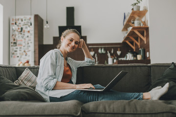 Smiling female sitting on couch with laptop