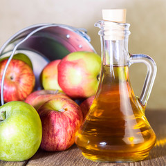 Processing of an agricultural crop of red and green apples. Home canning, healthy diet vegetarian food. Apple cider vinegar, juice, cider in a glass jug next to a bucket of ripe fruit