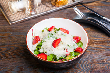 Fresh salad with strawberry, spinach and cheese in a bowl on wooden background. Served restaurant table with cutlery. Selective focus, Copy space.