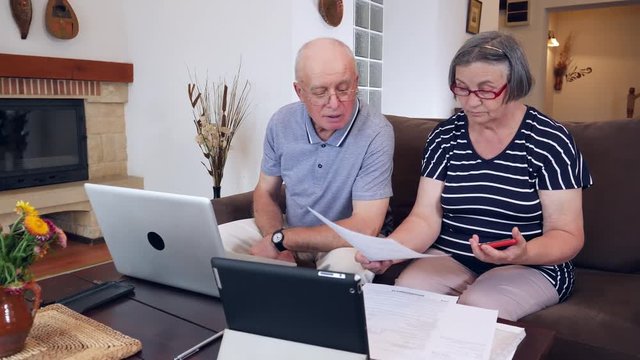 Nervous senior couple calculating the bills at home with laptop computer. Pensioners being frustrated by the costs of their bills. Handheld movement 4k slow motion