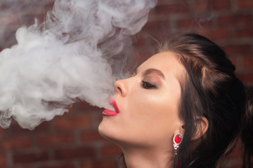 The girl with a make-up smokes an e-cigarette, lets out a lot of steam. Bad habits.