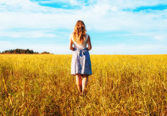 Young woman in wheat field. View from the back