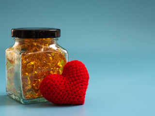 Red heart beside Fish oil capsules in glass bottles on blue background. Healthy omega-3 and stethoscope.