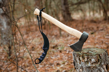 axe and karambit knife stuck in the stump in the forest
