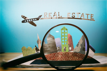 Magnifier in front of an open newspaper with paper houses. The concept of renting, searching,...