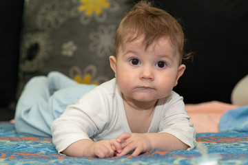 Baby boy is lying on tummy. The baby boy poses and looking at the camera.