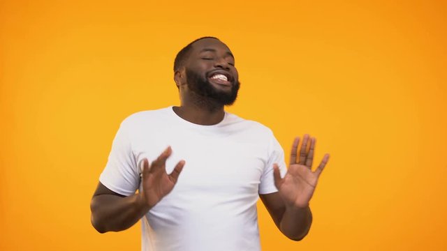 Happy and relaxed black man dancing against yellow background, looking at camera