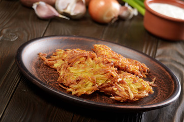 Fresh homemade tasty potato pancakes in clay dish on rustic wooden table