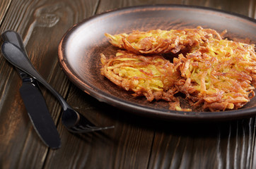 Fresh homemade tasty potato pancakes in clay dish on wooden table