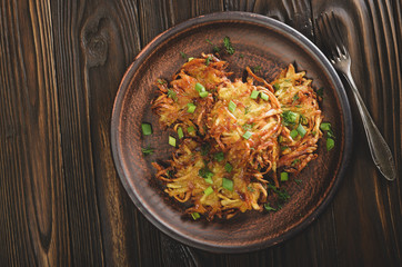 Top view of fresh homemade tasty potato pancakes in clay dish on wooden table