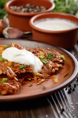 Homemade tasty potato pancakes in clay dish with sun-dried tomatoes and sour cream