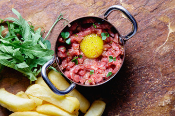 Carpaccio made of chopped tender veal with raw chicken eggs, served in a small metal pot on a stone...