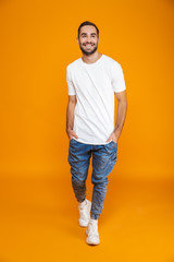 Fototapeta na wymiar Full length image of attractive guy 30s in t-shirt and jeans smiling while standing, isolated over yellow background