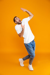 Full length image of frightened guy 30s in t-shirt and jeans raising hands while standing, isolated...