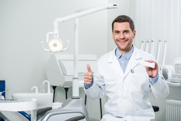 dentist holding toothpaste and showing thumb up in dental clinic