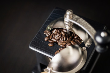 Close up of a rustic black wooden coffee grinder with roasted coffee beans with selective focus