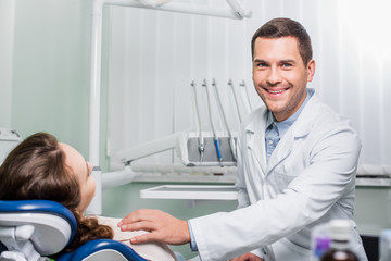 handsome dentist in white coat smiling near female patient