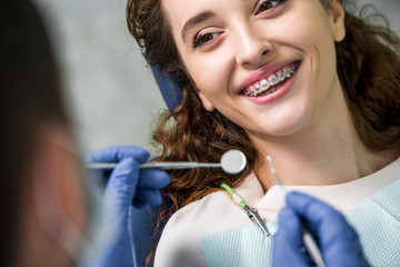 close up of cheerful woman in braces during examination of teeth near dentist