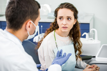 selective focus of sad woman looking at dentist in latex gloves and mask