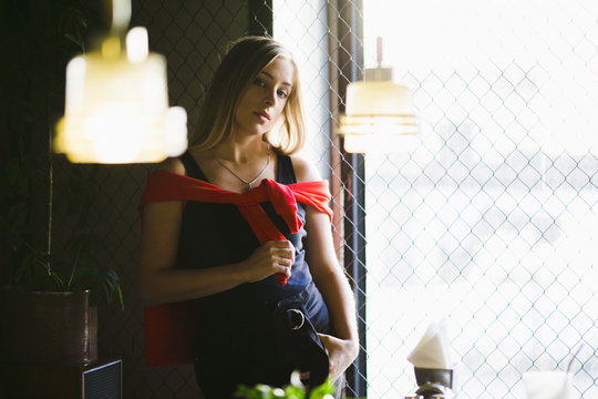 Streetstyle female portrait. Woman dressed in red shirt and sport pands sits in the dark room
