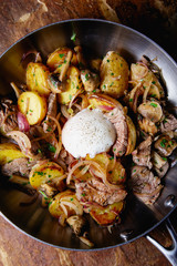 A delicious nourishing dinner of fried potatoes, meat, vegetables and soft chicken eggs served in a frying pan.