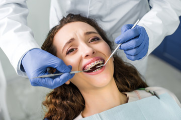 cropped view of dentist in latex gloves examining attractive woman in braces with opened mouth