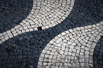 Shapes and patterns of a cobbled street of Lisbon (Portugal). Rounded and waving black and white shapes with an empty cobblestone space