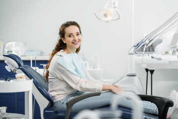 cheerful woman with braces on teeth smiling while sitting on chair in dental clinic