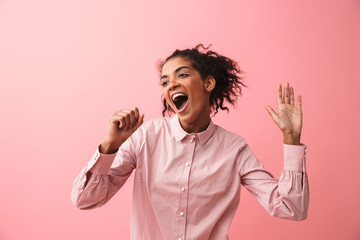 Beautiful young african woman posing isolated over pink wall background screaming singing.