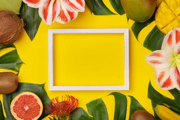 Creative flat lay with tropical fruits and plants and white frame for your text on yellow background