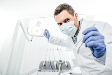 Fototapeta na wymiar dentist in latex gloves and mask holding dental lamp and dental instrument in hands