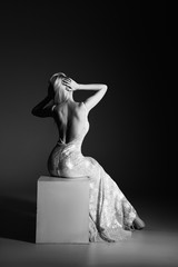 Fototapeta premium High fashion portrait of young elegant woman. Young lady in amazing silver glitter sequins luxury dress sitting on armchair Studio shot. Back view 