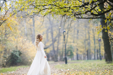 Fototapeta na wymiar Look from behind at charming bride whirling in autumn park covered with fallen leaves