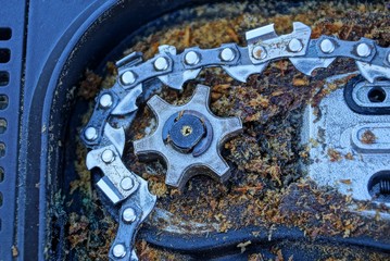 gray iron gear and chain in dirty sawdust in an electric saw