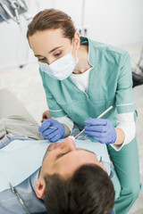 female dentist in mask holding dental instruments and examining patient in dental clinic
