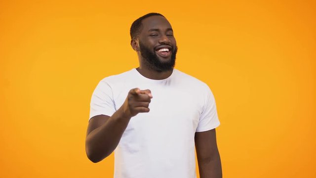 African american man pointing finger at camera and winking, smiling knowingly