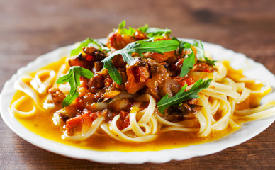 Sliced fried meat with vegetables and mushrooms in a sauce with bavette pasta in a plate on wooden table