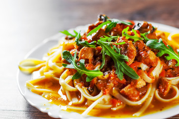 Sliced fried meat with vegetables and mushrooms in a sauce with bavette pasta in a plate on wooden table