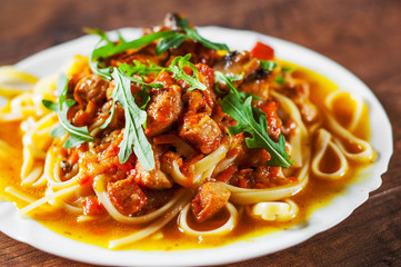 Sliced fried meat with vegetables and mushrooms in a sauce with bavette pasta in a plate on wooden table