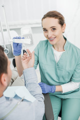 selective focus of attractive dentist smiling while holding toothpaste near patient