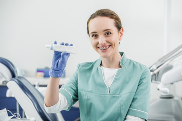 cheerful female dentist with braces on teeth holding toothpaste