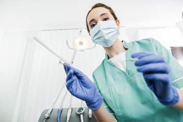 selective focus of dentist in mask and latex gloves holding dental instruments