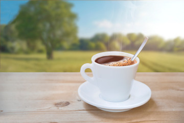 Cup of hot coffee on a natural wooden table against a landscape scene in the nature. Empty copy space for Editor's text.