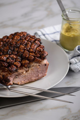 Deutscher Krustenbraten aus Schweinefleisch mit Senf auf Teller mit Küchenmesser und Fleischgabel auf Marmor Hintergrund