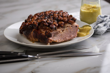 Deutscher Krustenbraten aus Schweinefleisch mit Senf auf Teller mit Küchenmesser und Fleischgabel auf Marmor Hintergrund