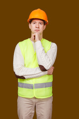 The serious man in a construction helmet and a vest, looks in the camera, the crossed hands at the head