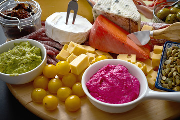 Antipasti board with different cheese and meat snacks with hummus and olives on wooden board