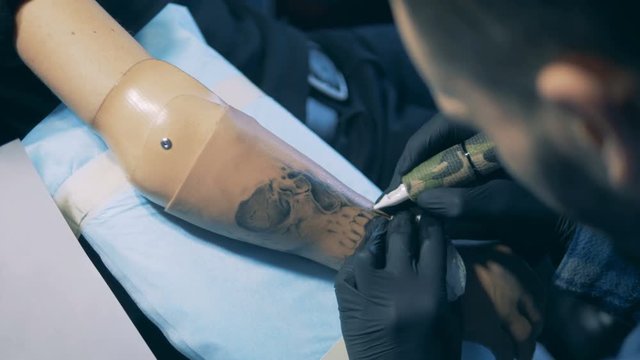 Black-ink tattoo is being made on a male prosthetic arm