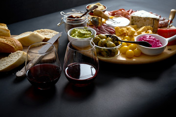 Antipasti board with cheese and meat snacks with red wine and baguette on board on black table