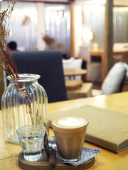 A glass of lot latte presented beautifully on a wooden tray with a pot of dried flowers in a cafe as background